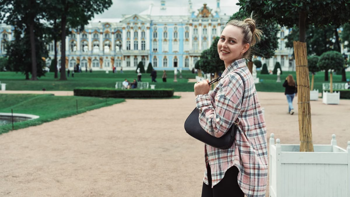 Young woman smiling in front of the Catherine Palace gardens, showcasing architecture.